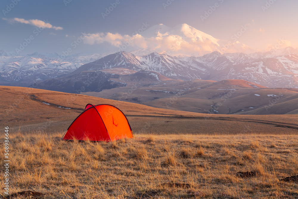 Golden light sunset with bright red tent in front of snow-covered Mount Elbrus, Caucasus, Russia