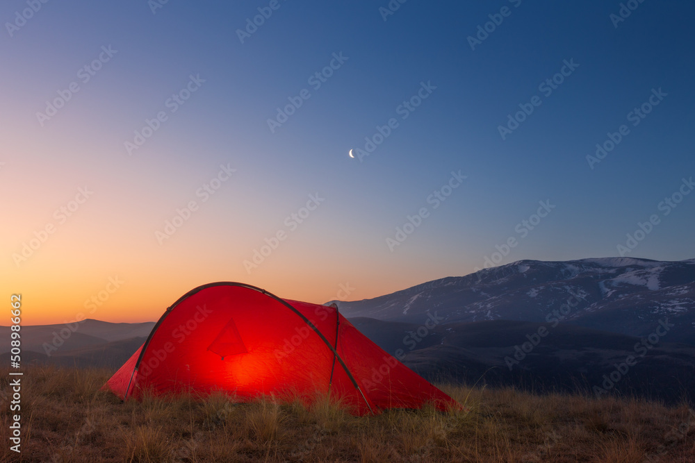 Sunrise landscape with bright tent in front of mountain ridge against colorful sky, Caucasus, Russia