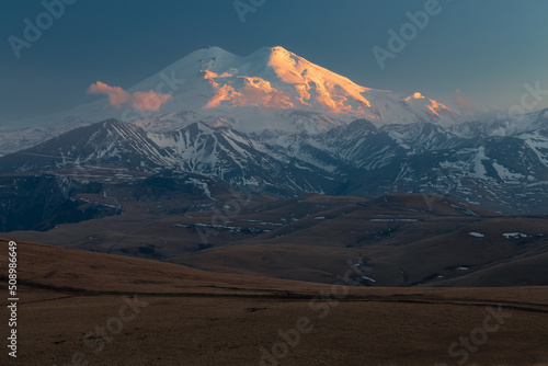 Landscape with snow-covered Mount Elbrus shining brightly in golden light of sunset  Caucasus Russia