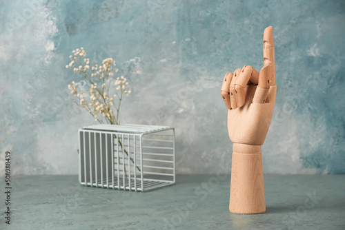 Wooden hand with raised index finger on blue background