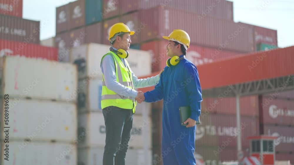 Asian cargo container workers stand in front of gate of workplace area and shake hands for the successful of project then they walk away. Asian cargo container workers stand in front of gate of workplace area and shake hands for the successful of project then they walk away.