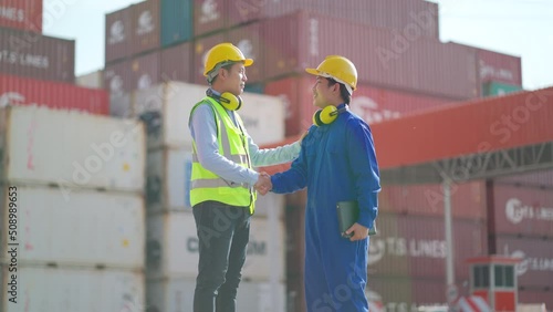 Asian cargo container workers stand in front of gate of workplace area and shake hands for the successful of project then they walk away.