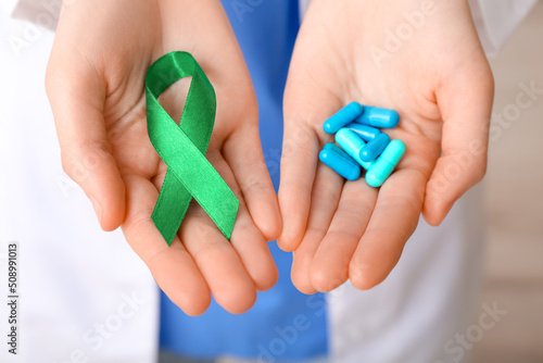 Female doctor with green ribbon and pills, closeup. Liver cancer concept