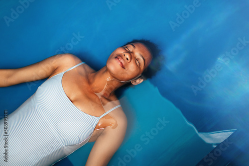 Billede på lærred Beautiful middle-aged African American woman floating in tank filled with dense salt water used in meditation, therapy and alternative medicine