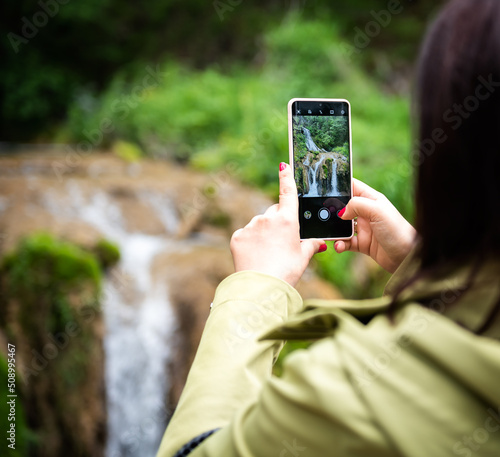 Female hands with red painted nails Taking Photo of a mountain Waterfall with Mobile Phone 