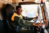 Young African American garbage removal worker driving a waste truck.