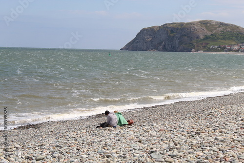 Fotografie A young couple in love are sitting on the pebble beach at Llandudno in North Wales