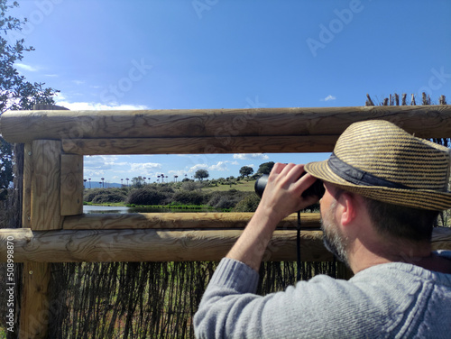 Hombre con prismáticos observando cigueñas en humedal (Malpartida de Cáceres, Extremadura, España) photo