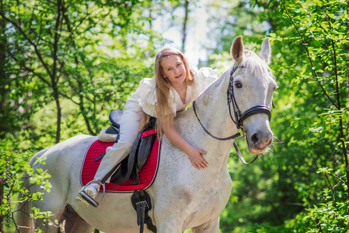 Teenage girl with her favorite white horse for a walk in the spring forest. Communication with animals in nature. Horizontal photographs of animals.
