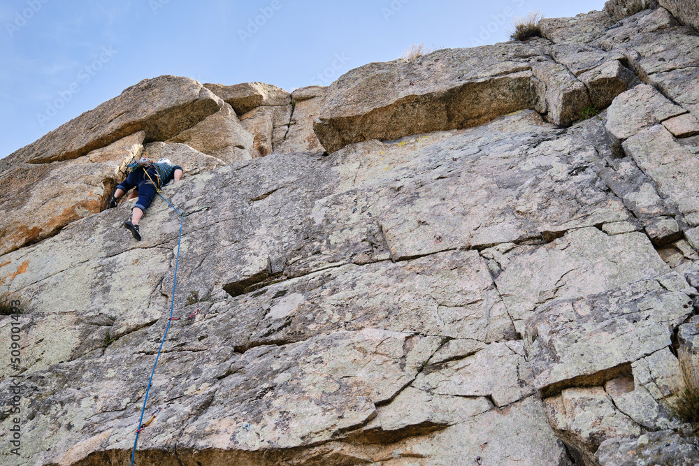 Man climbing up a vertical rock wall.