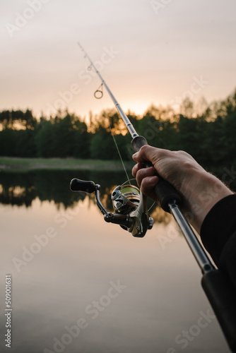 Fishing day. Fishing for pike, and perch from a lake, river or pond. Background wild nature. Fisherman with rod, spinning reel catches fish from a pier or boat. Article about concept of rural getaway.