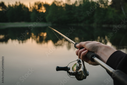 Fisherman with fishing rod, spinning reel on the background river bank. Sunrise. Fog against the backdrop of lake.