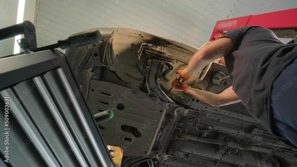 Young professional mechanic man working under lifted modern car in auto repair service. Car service, repair maintenance. Young professional mechanic man working under lifted modern car in auto repair service. Car service, repair maintenance.