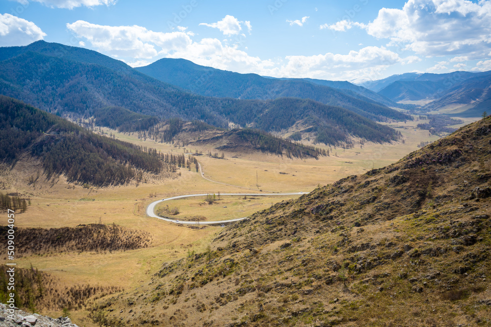 Scenic view from mountain pass to forest valley among mountain ranges and hills on horizon at changeable weather in spring time in Altai, Russia