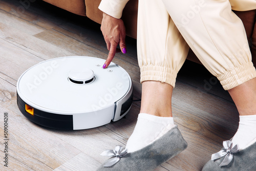 Woman switches on robot vacuum cleaner sitting on sofa photo