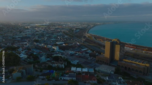 Fly around high rise post office building lit by setting sun. Aerial footage of city at sea bay. Port Elisabeth, South Africa