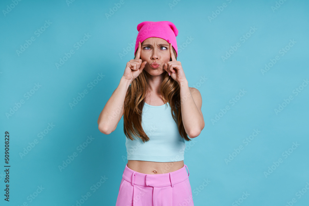 Playful young woman in pink hat grimacing while standing against blue background Playful young woman in pink hat grimacing while standing against blue background