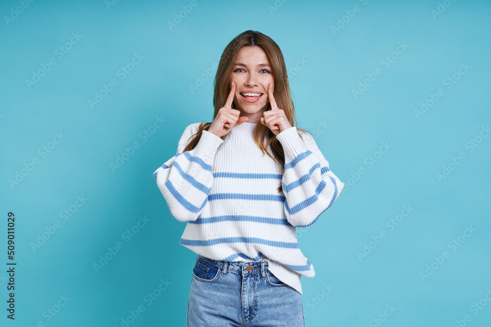 Beautiful young woman looking at camera and smiling while standing against blue background Beautiful young woman looking at camera and smiling while standing against blue background