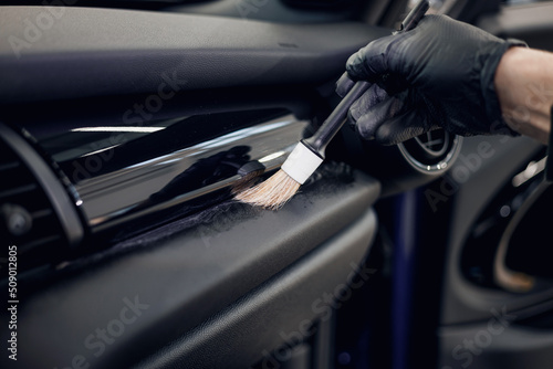 Cleaning the car interior with a brush. Auto detailing worker cleaning car interior, car detailing concept. Selective focus. Dust removal from the dashboard of the car with a brush