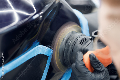 Professional car polishing. Worker with orbital polisher in auto repair shop. Car detailing, car wash, and paint correction concept. Random orbital polisher background