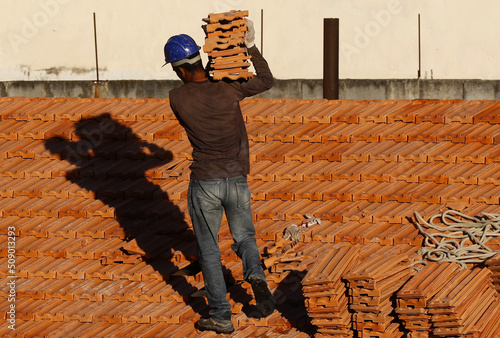 Roofer working on roofing construction. Bricklayer roof repair. House under construction. Workman renovates waterproofing roof of building. Carpenter construction worker carry pile of tiles