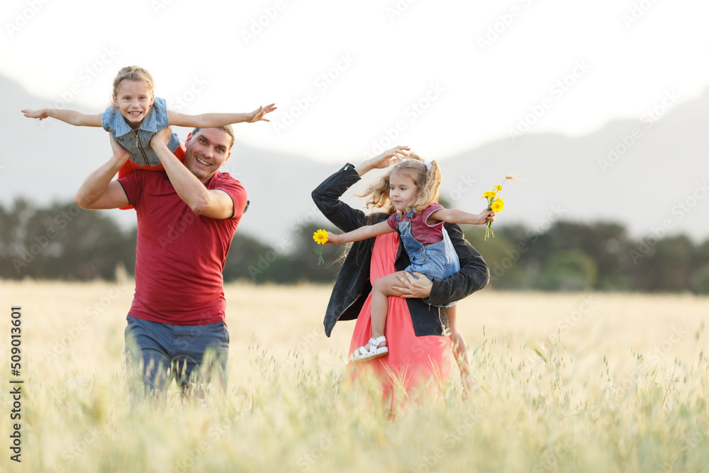 Happy family father of mother and two daughters sisters on nature at sunset.Carefree parents having fun with their kids on a field.