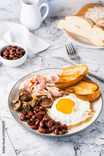 English breakfast with fried egg, bacon, beans, mushrooms and toast on a plate. Vertical view