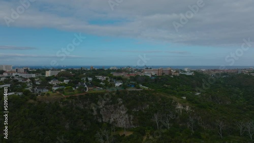 Aerial view of luxury residences above steep escarpment. Urban borough surrounded by green vegetation and sea in background. Port Elisabeth, South Africa