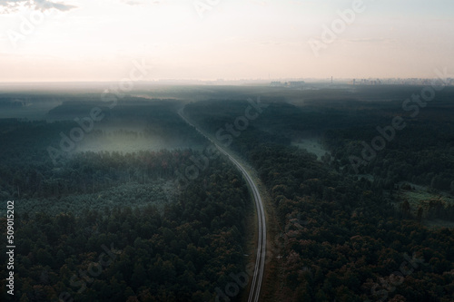 Railway goes into the distance in a mysterious misty forest - an aerial drone shot. Rails of the railway among the mysterious mystical forest