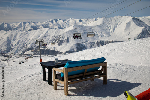 Chair at mountains in winter, relaxing in a cafe in the sun in front of winter mountains and a village panorama