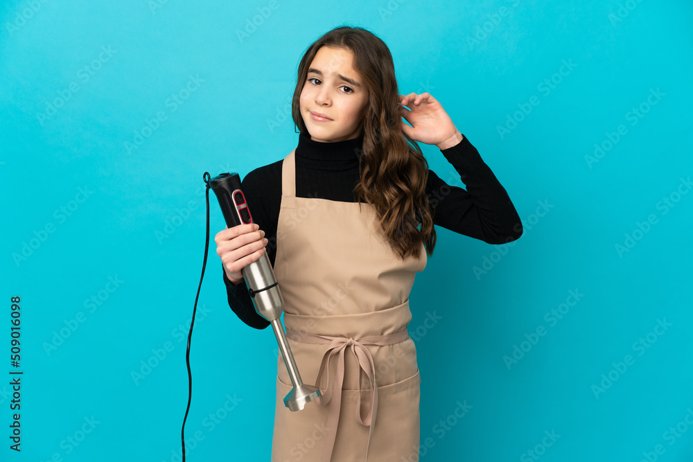 Little girl using hand blender isolated on blue background having doubts Little girl using hand blender isolated on blue background having doubts
