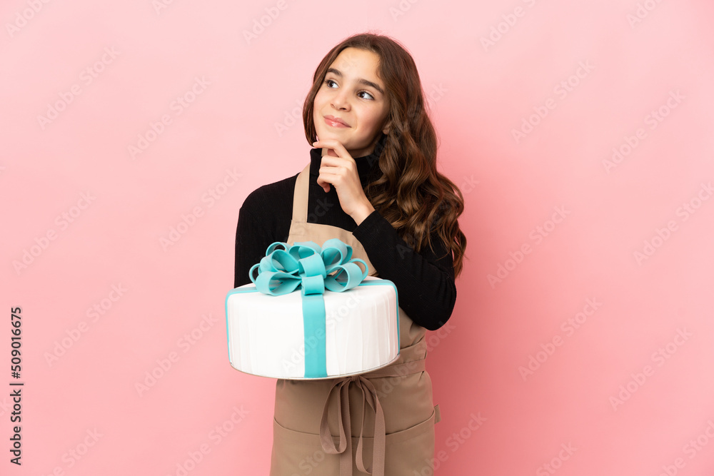 Little Pastry chef holding a big cake isolated on pink background having doubts and thinking Little Pastry chef holding a big cake isolated on pink background having doubts and thinking