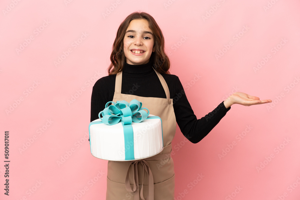 Little Pastry chef holding a big cake isolated on pink background with shocked facial expression Little Pastry chef holding a big cake isolated on pink background with shocked facial expression