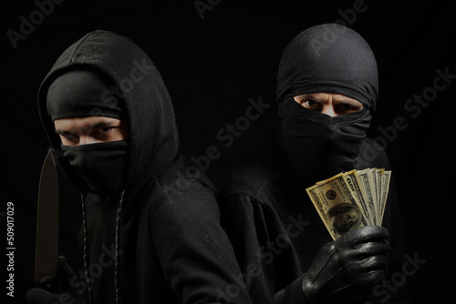 Photo thieves in black masks with a knife and dollars in their hands on a black background