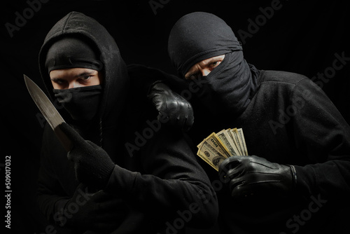 Fotografie, Obraz thieves in black masks with a knife and dollars in their hands on a black background