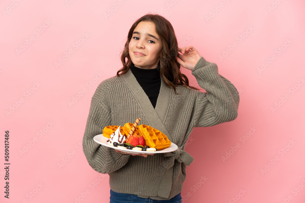 Little girl holding waffles isolated on pink background having doubts Little girl holding waffles isolated on pink background having doubts