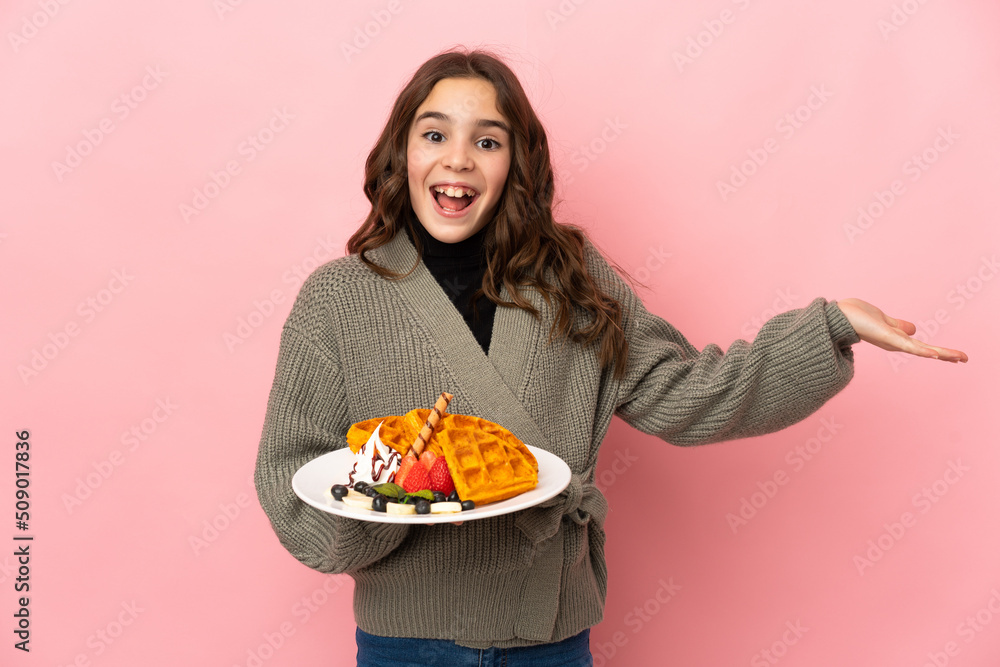 Little girl holding waffles isolated on pink background with shocked facial expression Little girl holding waffles isolated on pink background with shocked facial expression