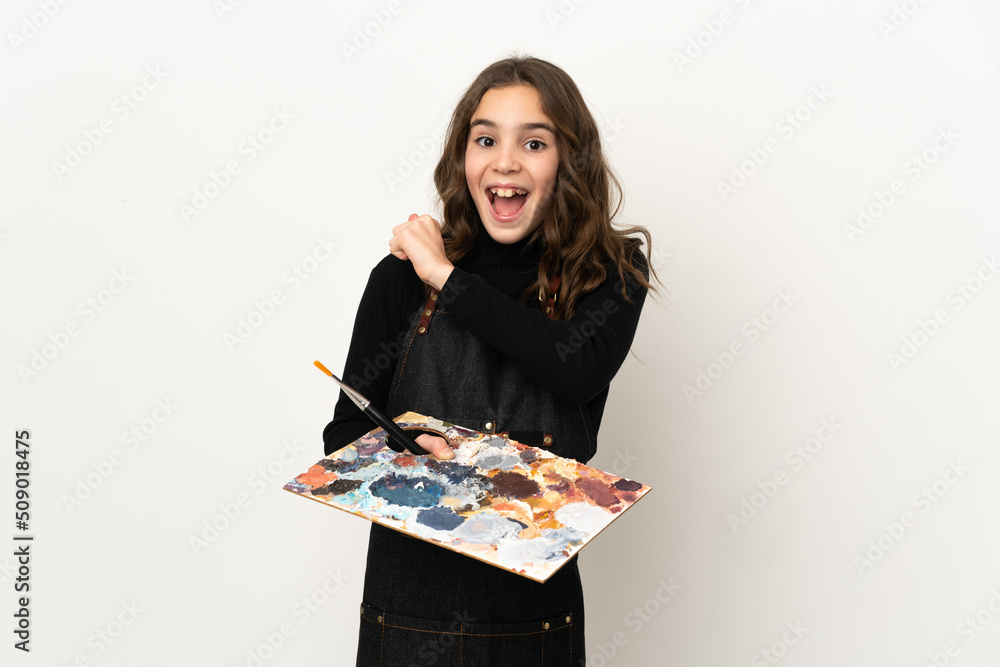 Little artist girl holding a palette isolated on white background celebrating a victory Little artist girl holding a palette isolated on white background celebrating a victory