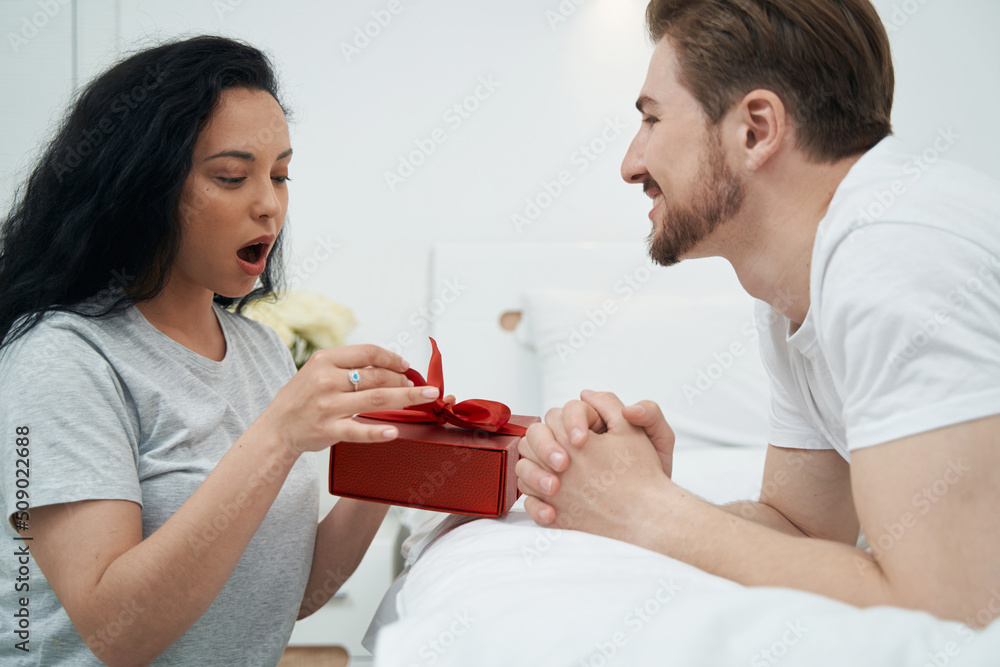 Man observing astonished woman opening his present Man observing astonished woman opening his present