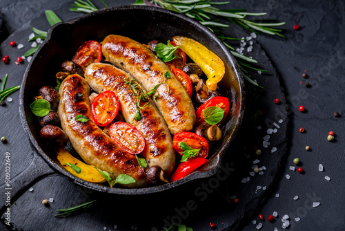 Grilled sausages and vegetables with herbs in iron pan