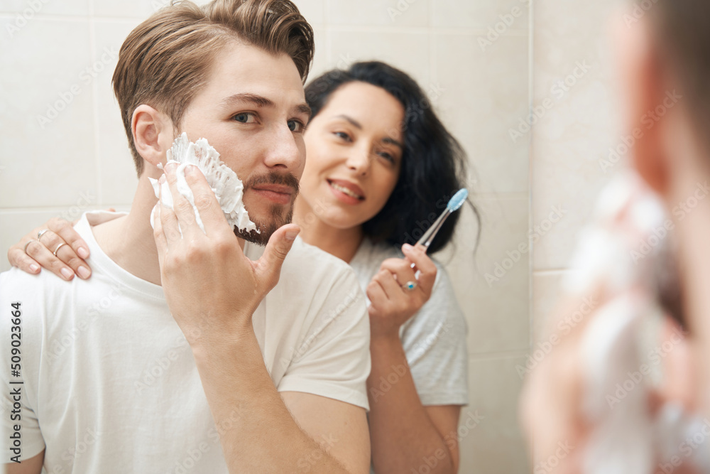 Young family couple standing before bathroom mirror Young family couple standing before bathroom mirror