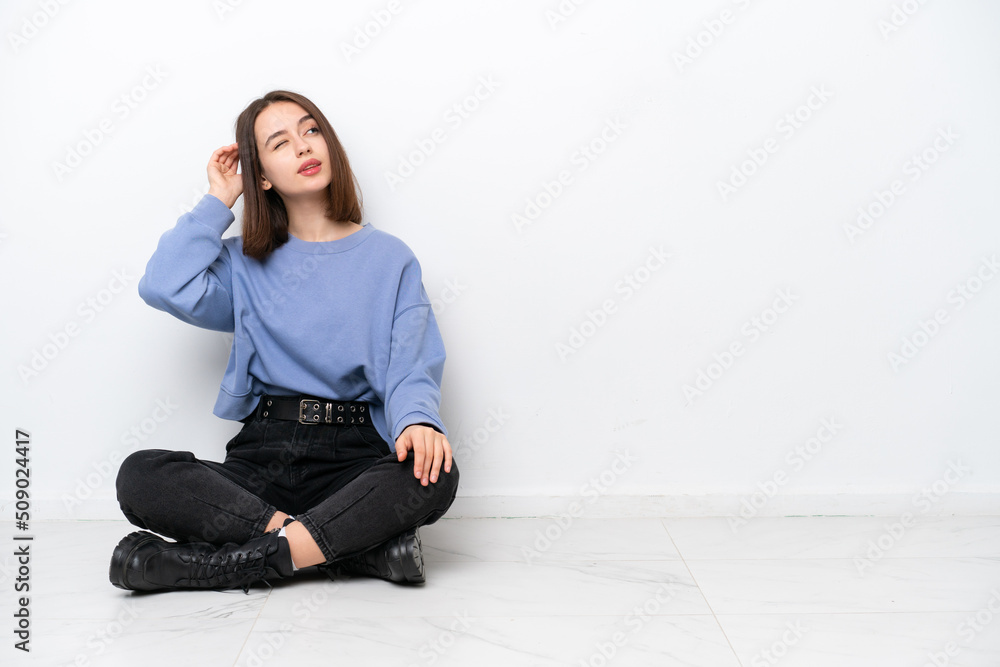 Young Ukrainian woman sitting on the floor isolated on white background having doubts and with confuse face expression Young Ukrainian woman sitting on the floor isolated on white background having doubts and with confuse face expression