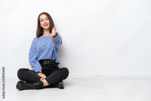 Young Ukrainian woman sitting on the floor isolated on white background shaking hands for closing a good deal