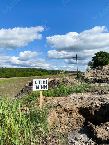 War in Ukraine. Minefield. Mines. Sign caution, stop, mines in Ukrainian. Danger, mines. Russian aggression. Green field, power line, grass and forest during the war
