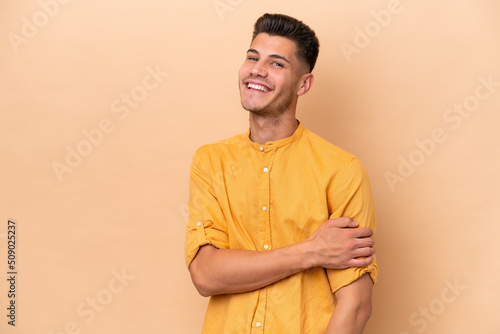 Young caucasian man isolated on beige background laughing