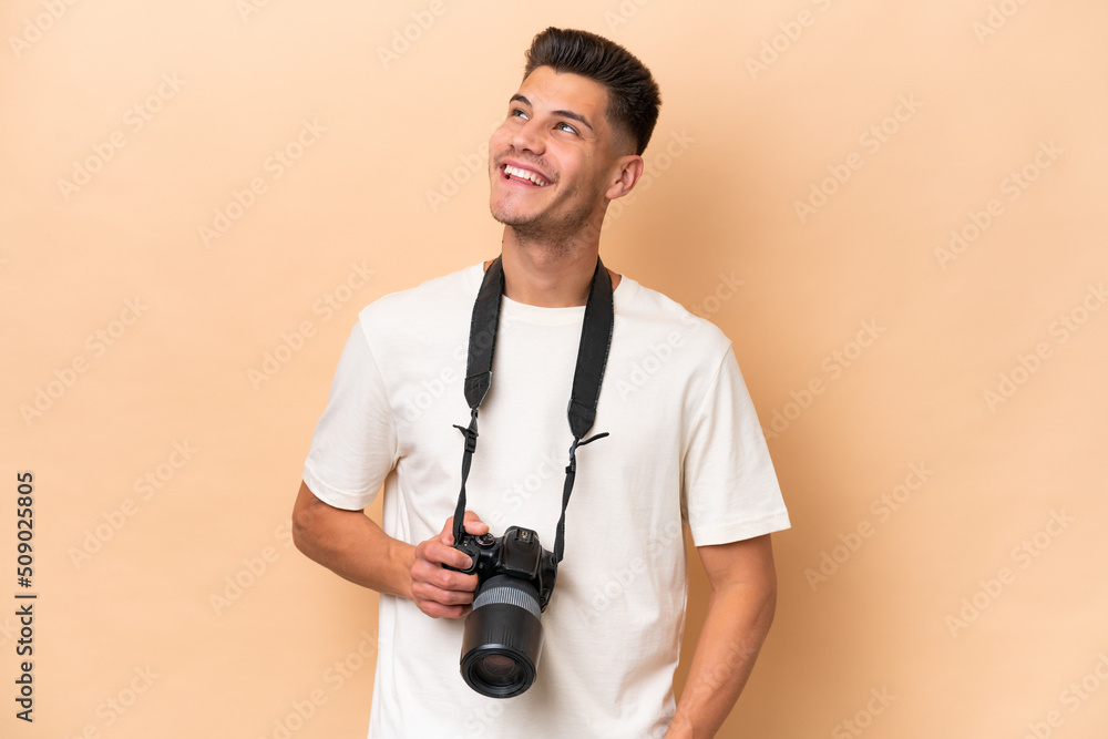 Young photographer caucasian man isolated on beige background looking up while smiling Young photographer caucasian man isolated on beige background looking up while smiling