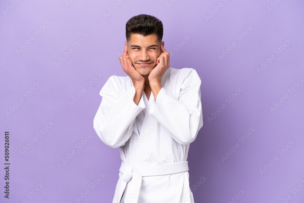 Young caucasian man doing karate isolated on purple background frustrated and covering ears