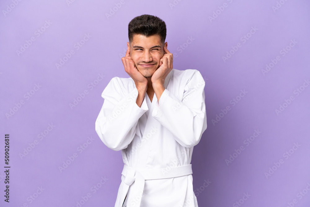 Young caucasian man doing karate isolated on purple background frustrated and covering ears Young caucasian man doing karate isolated on purple background frustrated and covering ears