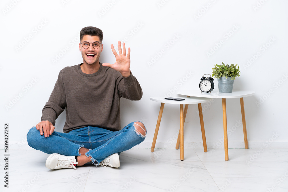 Young caucasian man sitting in his home isolated on white background counting five with fingers Young caucasian man sitting in his home isolated on white background counting five with fingers