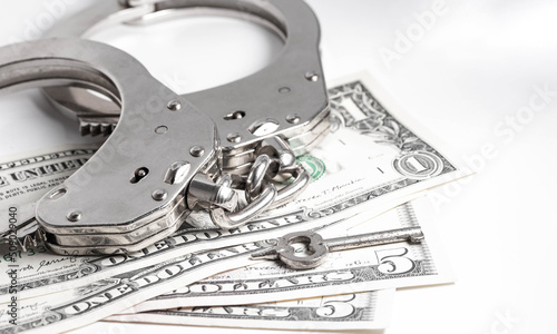 Police handcuffs with a key are on the low denomination USD bills. Minor crimes. Police handcuffs, the penalty of imprisonment for a crime.